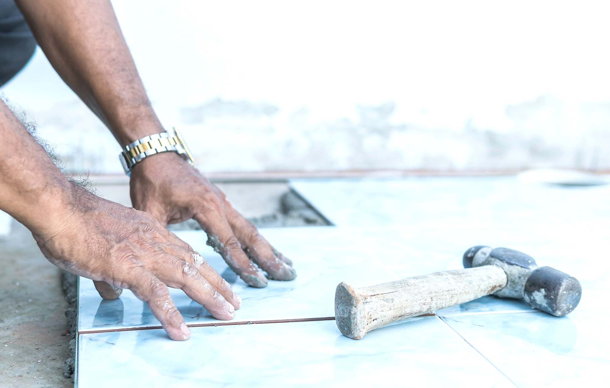 Hand worker flooring ceramic tile and hammer